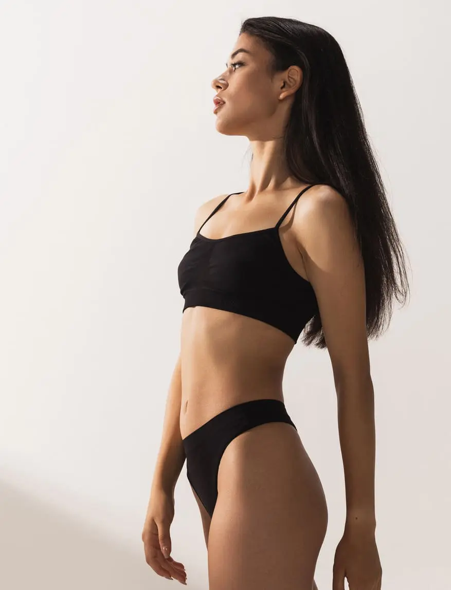 Studio image of young beautiful woman with slim figure in black underwear posing over white studio background Tummy Tuck in Charleston County, SC